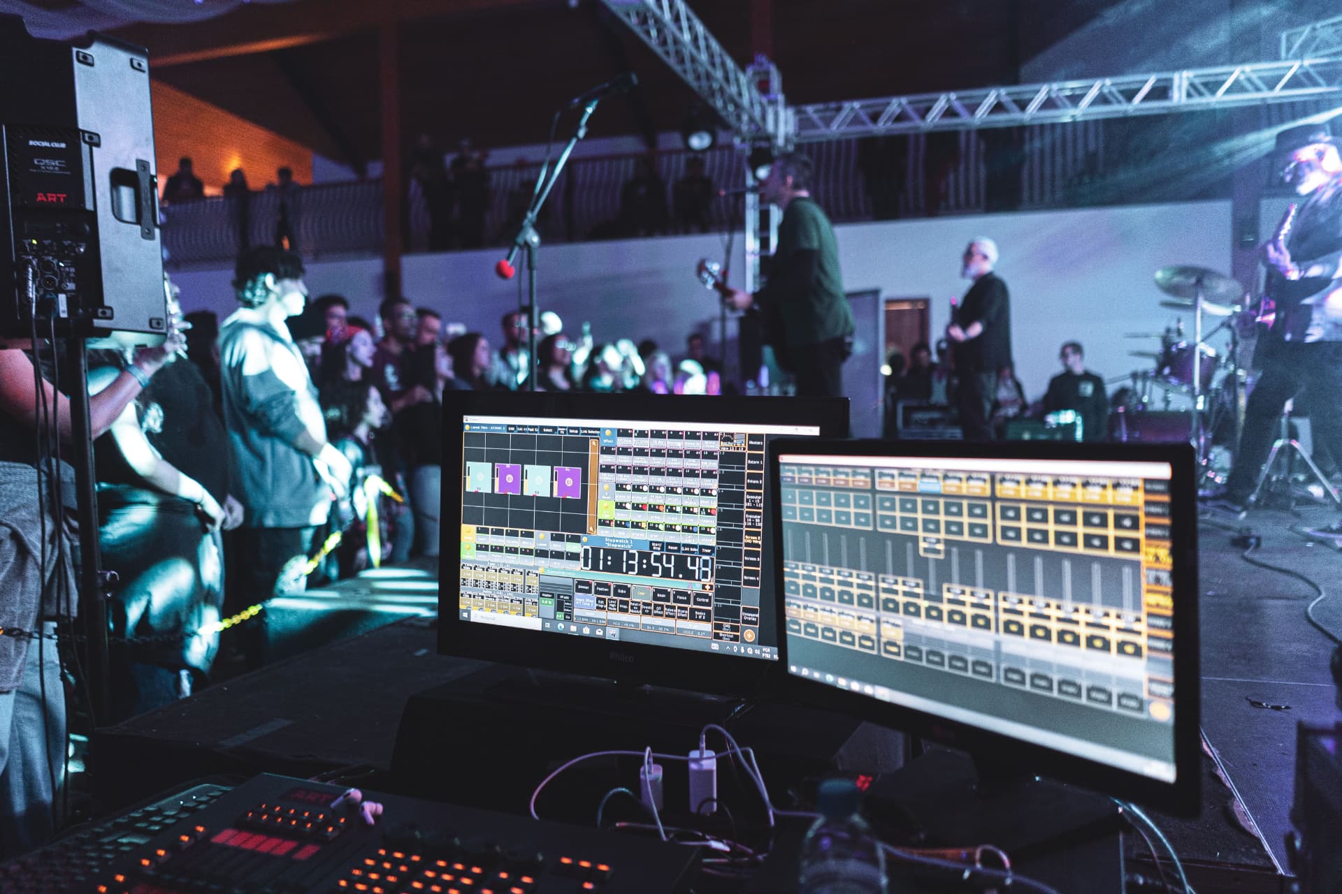 Live mix in progress from behind the mixing station, dual monitors facing a lit stage